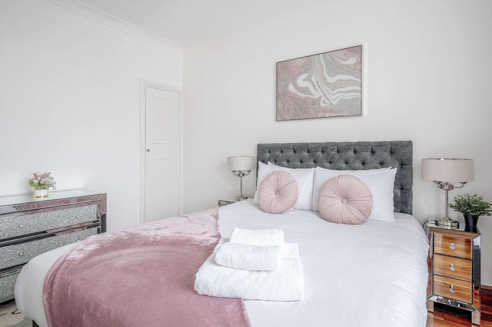 A neatly arranged bedroom with a bed, bedside tables, a dresser, and a wall-mounted artwork.