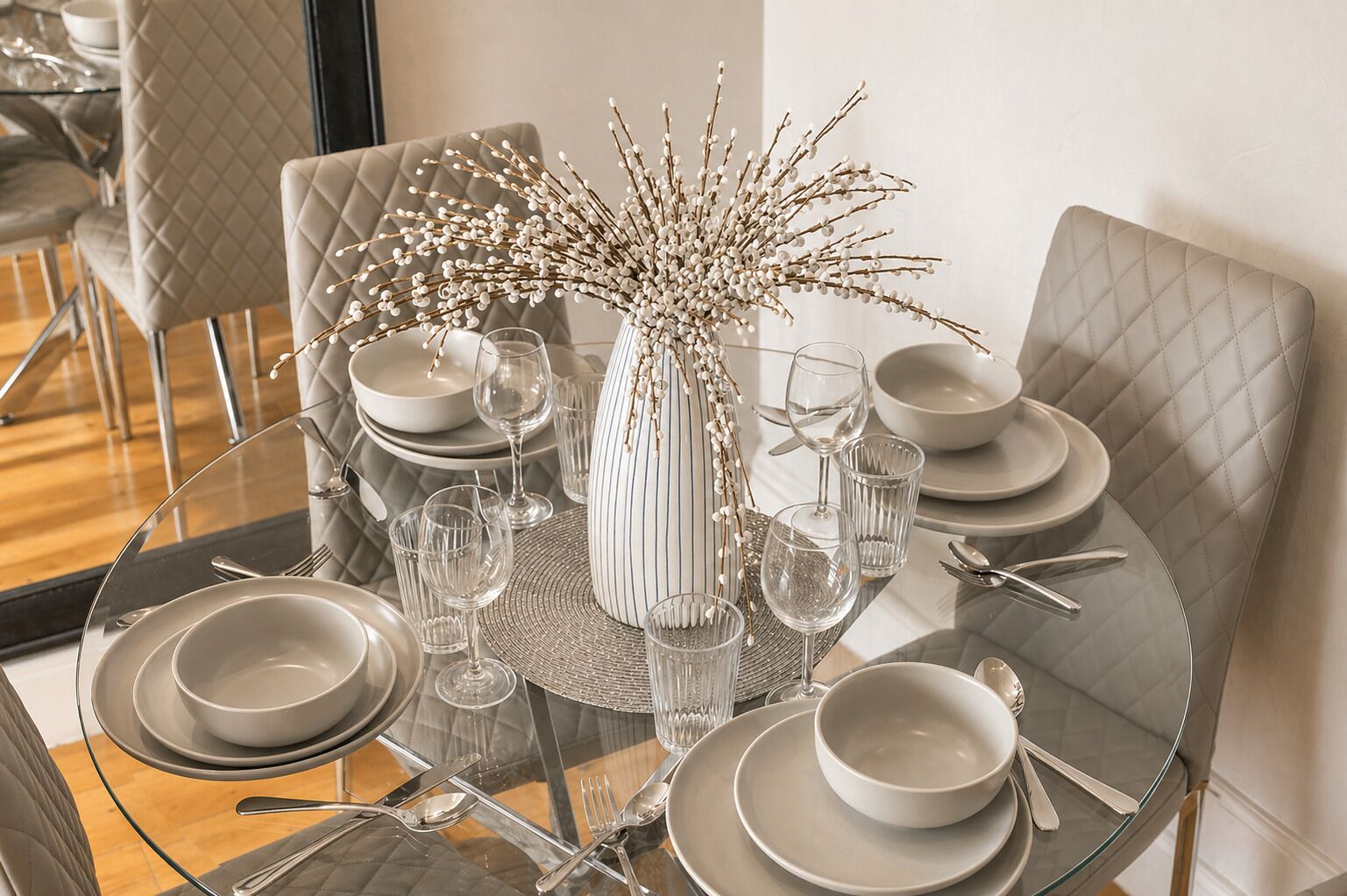 A dining table set with plates, glasses, and cutlery, surrounded by cushioned chairs.
