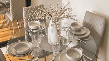 A dining table set with plates, glasses, and cutlery, surrounded by cushioned chairs.
