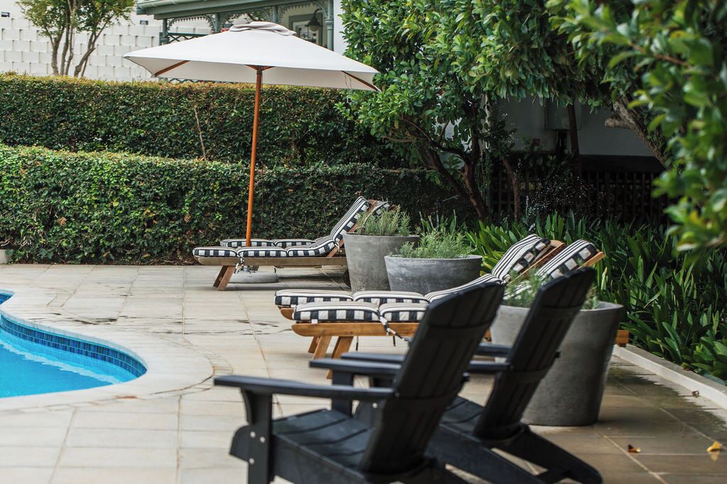 A poolside area with lounge chairs, a large umbrella, and potted plants.