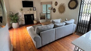 Un salon avec une cheminée, un canapé gris, un plancher en bois et un téléviseur fixé au mur.
