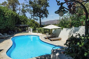 Une piscine avec des chaises longues, une pergola et une vue sur les montagnes.