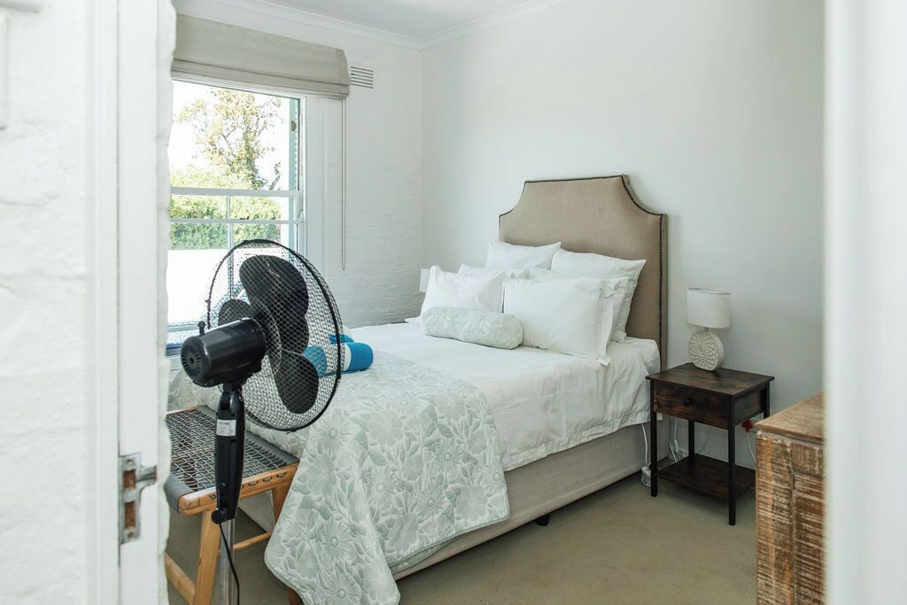 A bedroom with a bed, a standing fan, a nightstand, and a window.