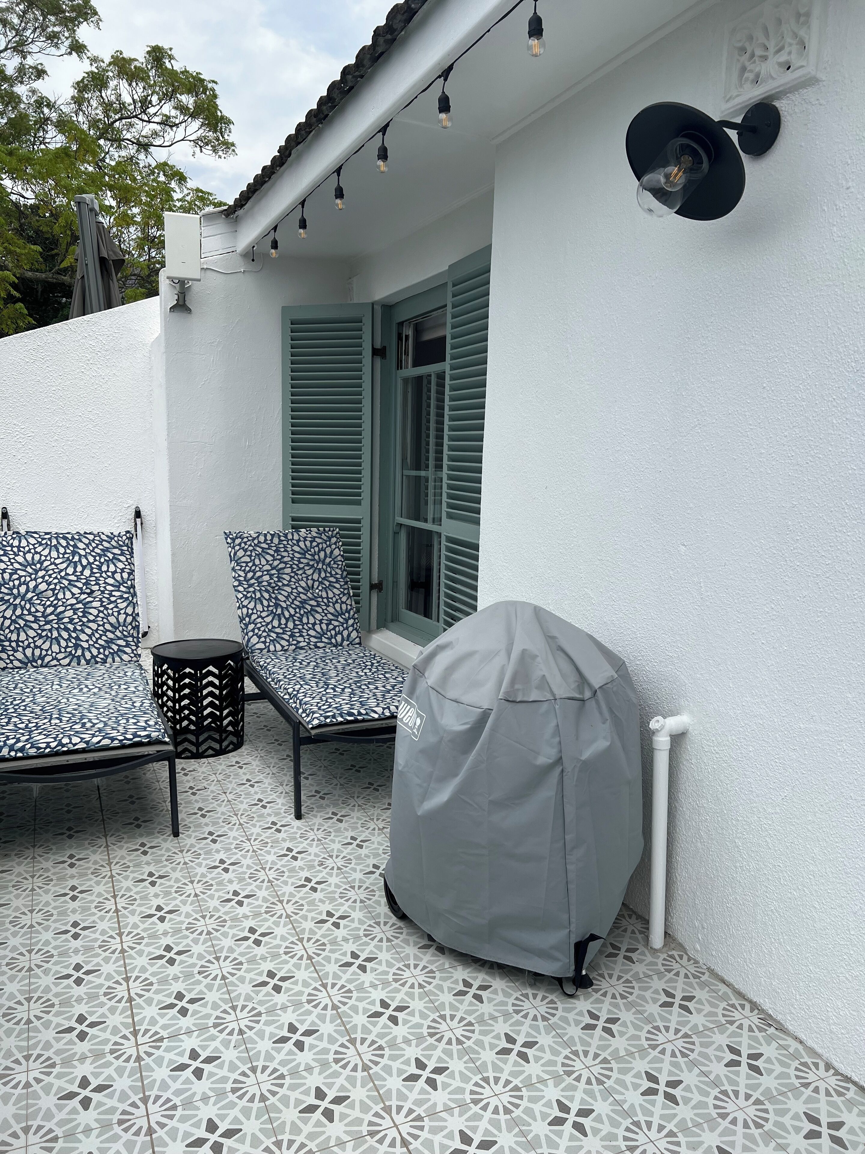 Eine Terrasse mit gemusterten Gartenmöbeln, einem Grill und Lichterketten.