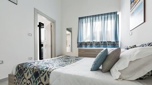 Ein Schlafzimmer mit Bett, Fenster mit Vorhängen, einer Tür und einem an der Wand befestigten Lichtschalter.