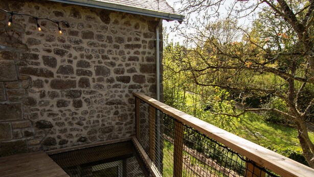 Ein Steinhaus mit einer Holzterrasse und einem Metallzaun.