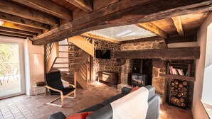 Ein rustikales Interieur mit Kamin aus Stein, Holzbalken, einer Couch und einem Fernseher.