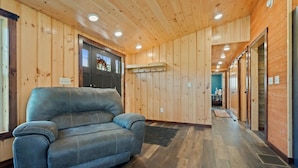 Una habitación con paredes y techo de madera, un sofá gris y una puerta con ventanal.