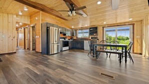 Una cocina amplia con pisos de madera, un comedor con mesa y sillas, y ventanas grandes que ofrecen vistas al exterior.