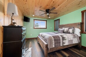 A bedroom with a wooden ceiling, a bed with a patterned blanket, a dresser, and a ceiling fan.