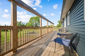 A wooden deck with a railing, a table with chairs, and a view of a green landscape.
