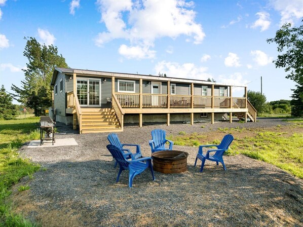 A two-story wooden cabin with a deck, outdoor seating, and a fire pit.