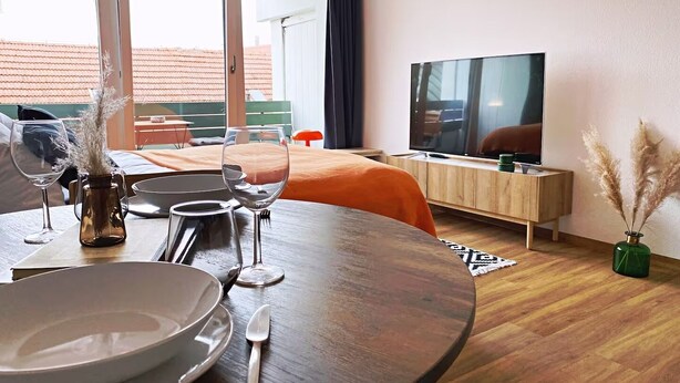 Ein modernes Hotelzimmer mit Essbereich, Fernseher und Balkon mit Blick auf die Stadt.