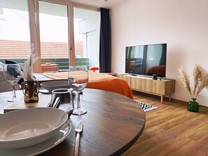 A modern hotel room with a dining area, a TV, and a balcony with a view of the cityscape. - Old town apartment near the cathedral (Augsburg)
