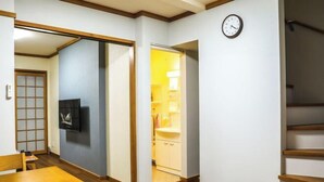 Habitación con piso de madera, televisor montado en la pared, un reloj y una puerta corredera que da al baño.
