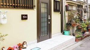 Un edificio residencial con una puerta marrón, un letrero pequeño en la pared y plantas en macetas en la acera.