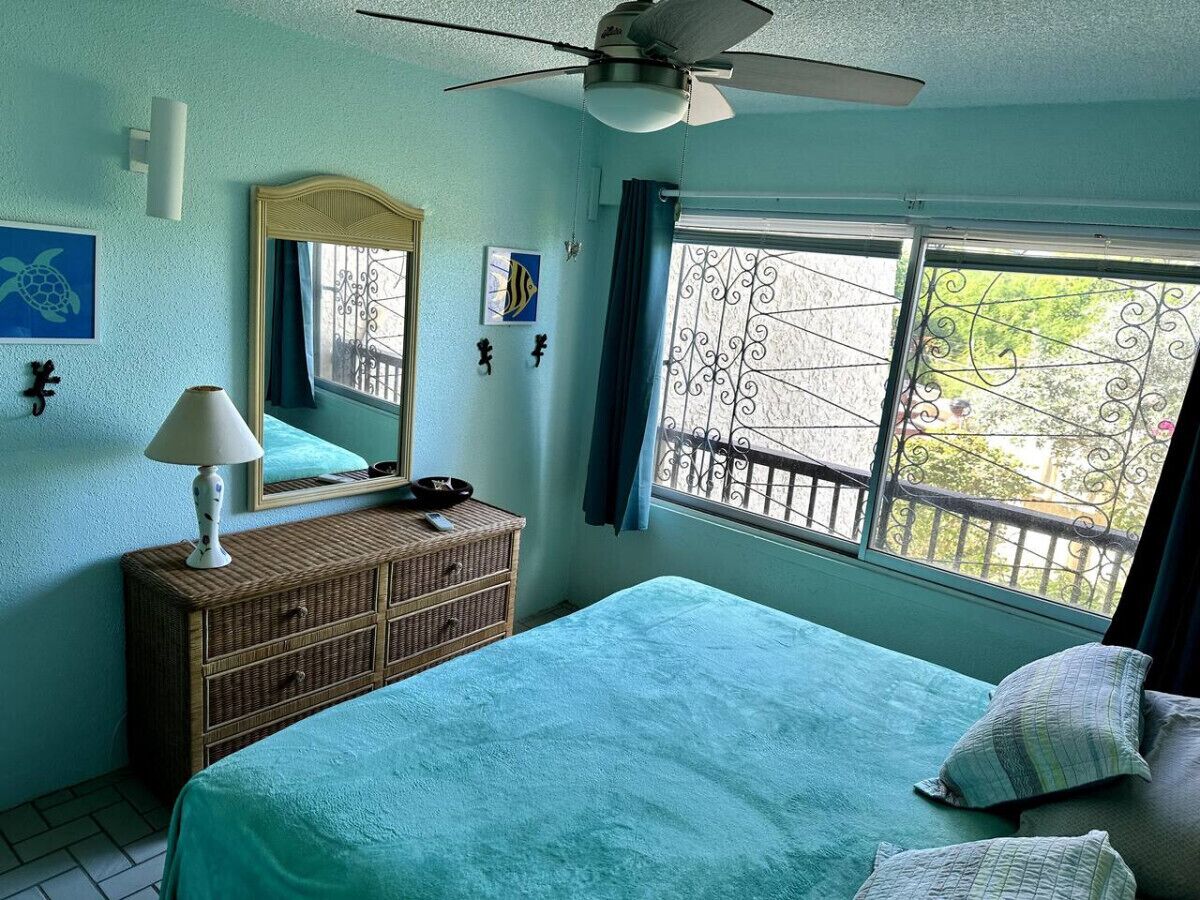 A bedroom with a bed, a dresser, a ceiling fan, a window with a view, and wall decorations.