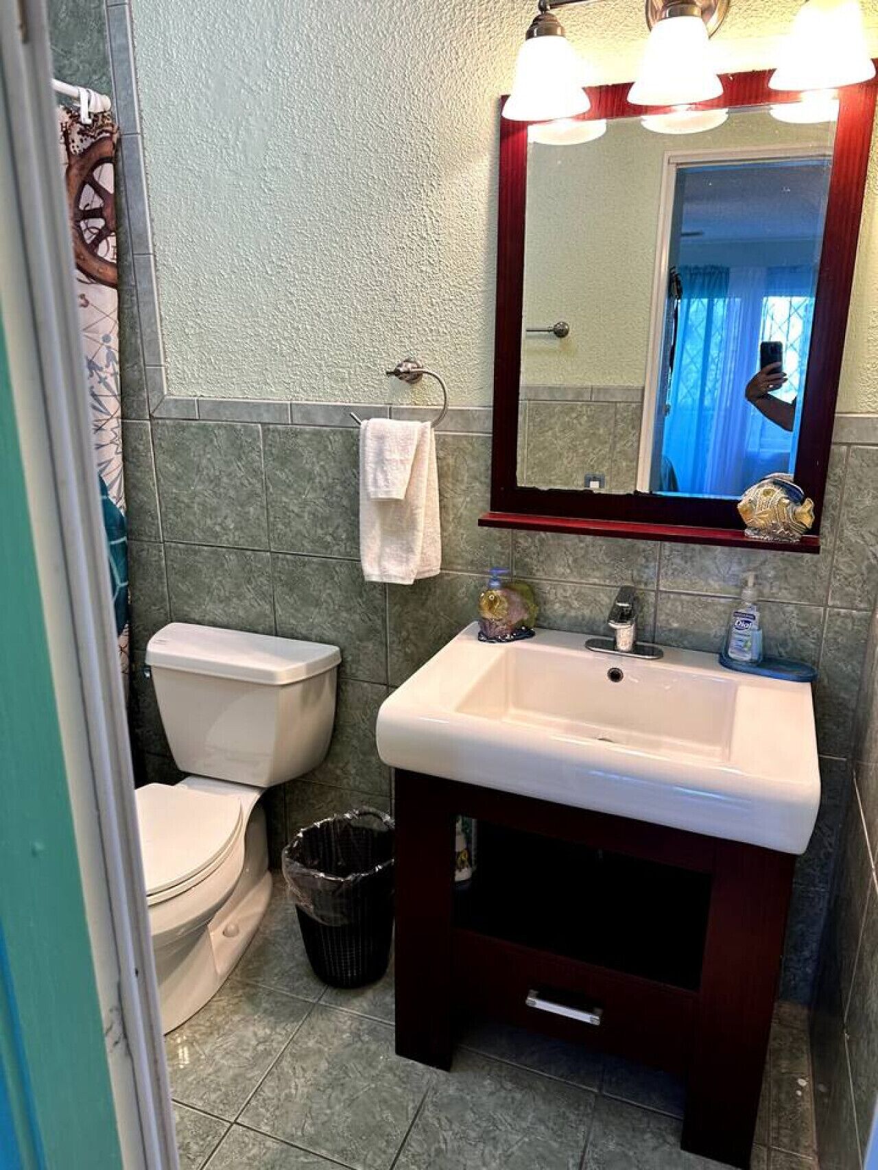 Une salle de bain avec des toilettes blanches, un lavabo surmonté d’un miroir et une serviette suspendue à un porte-serviettes.
