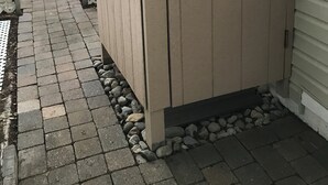 A wooden shed with a sliding door, a brick pathway, and a small rock border.