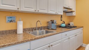 A kitchen with white cabinets, a granite countertop, a stainless steel sink, a kettle, and a coffee maker.