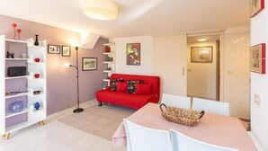 A modern living room with a red sofa, white shelves, and a dining area with a table and chairs.