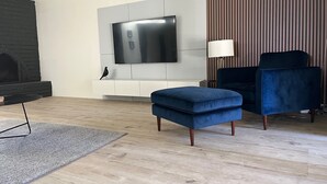 A modern living room with a flat-screen TV mounted on a white wall, a blue velvet armchair, a matching ottoman, a black fireplace, and a striped wallpaper accent. - Walk to Spring Training  - 3BR home in Scottsdale (Scottsdale)