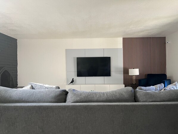 A modern living room with a grey sofa, a flat-screen TV mounted on a white wall, a dark blue armchair, and a striped wallpaper pattern. - Walk to Spring Training  - 3BR home in Scottsdale (Scottsdale)