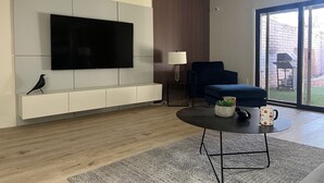 A modern living room with a flat-screen TV mounted on a white wall, a dark blue sofa, a small round coffee table with a plant and mug, and a sliding glass door leading to a backyard. - Walk to Spring Training  - 3BR home in Scottsdale (Scottsdale)