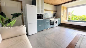Una cocina moderna con horno empotrado, microondas y lavadora, un sofá beige y un ventanal con vistas a zonas verdes.