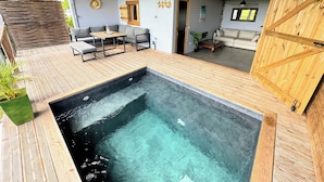 Un espacio al aire libre moderno con terraza de madera, jacuzzi y zona de estar con mesa y sillas.