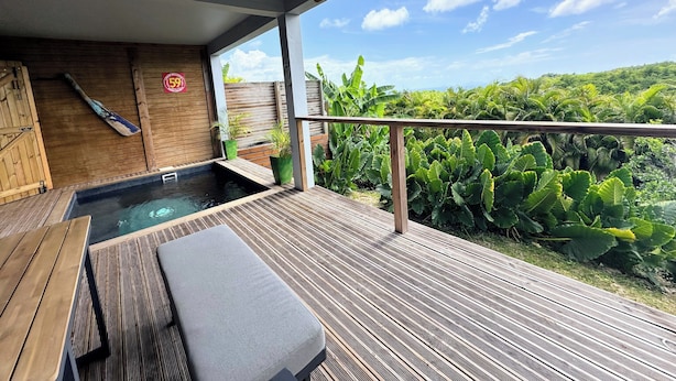 Una terraza de madera con un jacuzzi, un banco y vistas de vegetación exuberante.