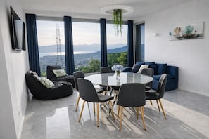 Un salon moderne avec une table ronde en verre, des canapés foncés et une vue sur la ville.