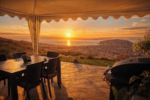 Une terrasse extérieure avec une table et des chaises, un barbecue et une vue sur le paysage urbain au coucher du soleil.