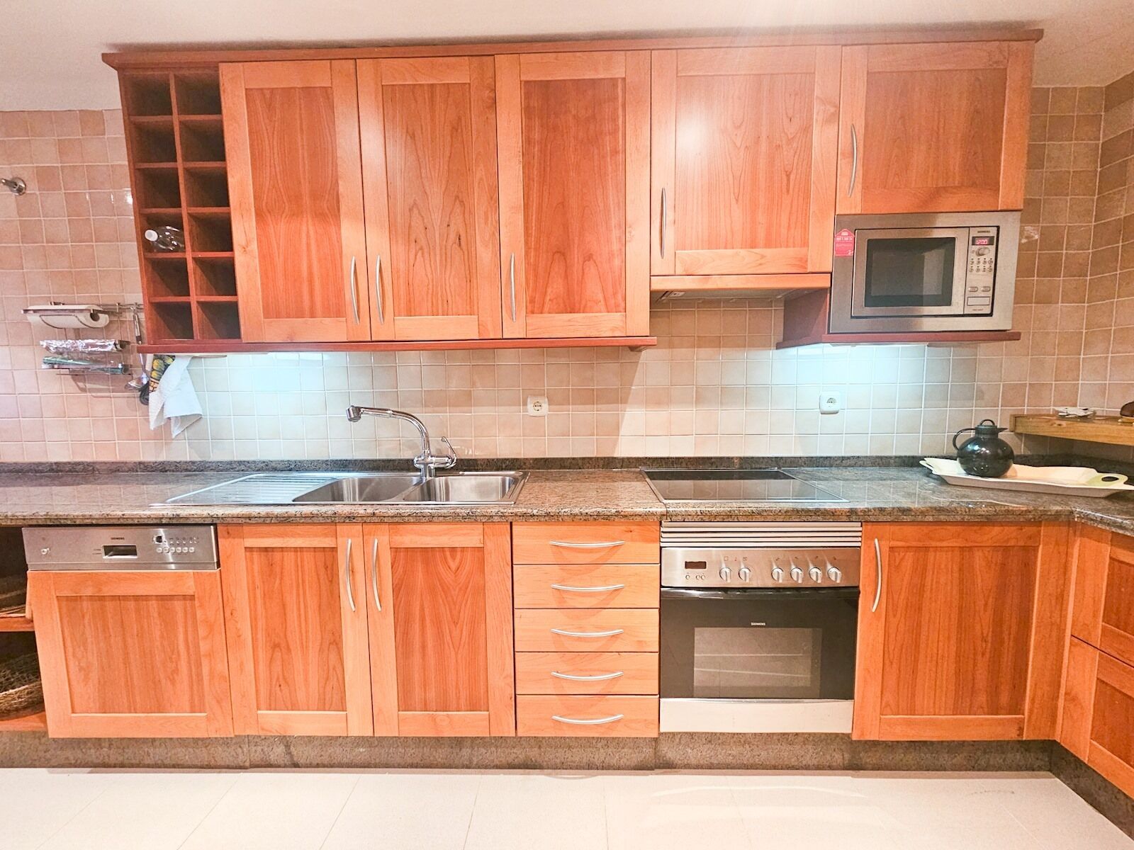 A kitchen with wooden cabinets, a stainless steel sink, a microwave, and an oven.