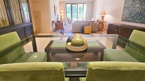 A spacious living room with a glass coffee table, green upholstered chairs, a sofa, and a dining area with a buffet table. - Beachfront Apartment in San Pedro - Pass the Keys (Marbella)