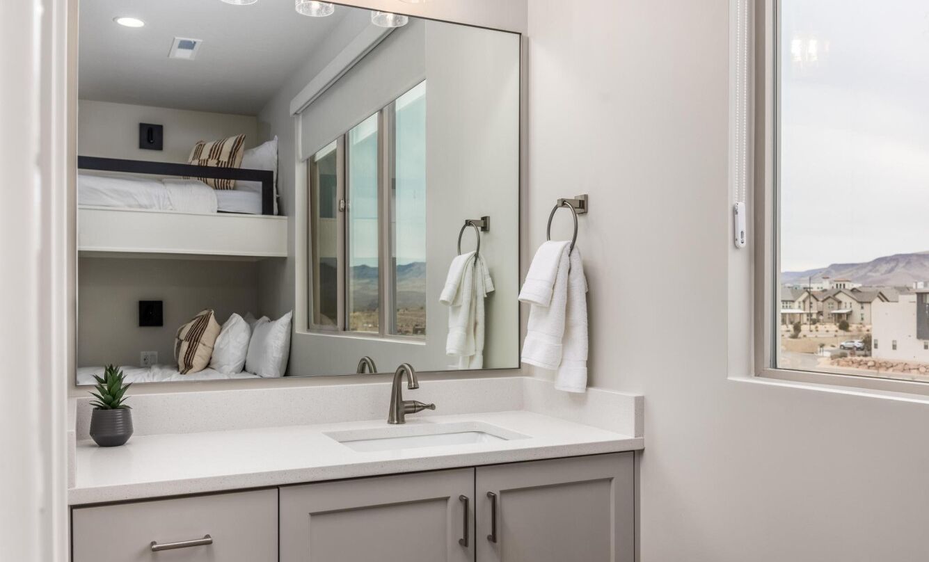 A modern bathroom with a large mirror, a sink, and a window offering a view of a residential area.