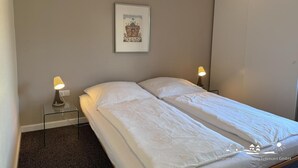 Una cama individual con ropa blanca, dos lámparas de noche, un cuadro enmarcado en la pared y un armario.