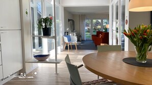 Una cocina moderna con estufa integrada, una zona de comedor con mesa redonda y vistas al jardín a través de amplias ventanas.