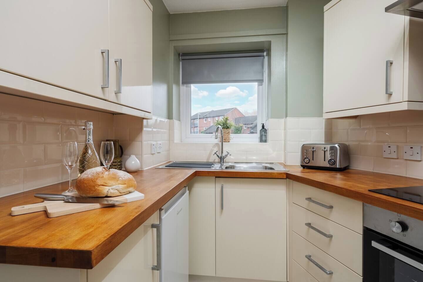 Une cuisine moderne avec des meubles blancs, un plan de travail en bois, un grille-pain et une fenêtre donnant sur des maisons.