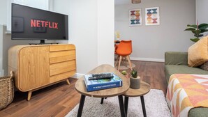 A modern living room with a wooden cabinet, a television displaying 'NETFLIX', a small table with a book, and a sofa.