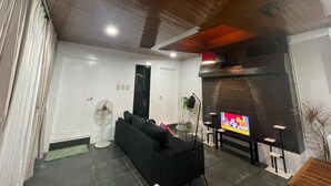 A living room with a black sofa, a TV, a fireplace, and a ceiling fan. - Ocean View (Naval)