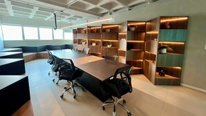 A modern conference room with a long table, black office chairs, and built-in wooden shelving with plants. - RN STUDIO APTO 904 (Maceió)