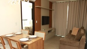 A dining area with a wooden table and chairs, a sofa, and a TV mounted on the wall. - Edificio Liv P. Verde Apt 706 (Maceió)