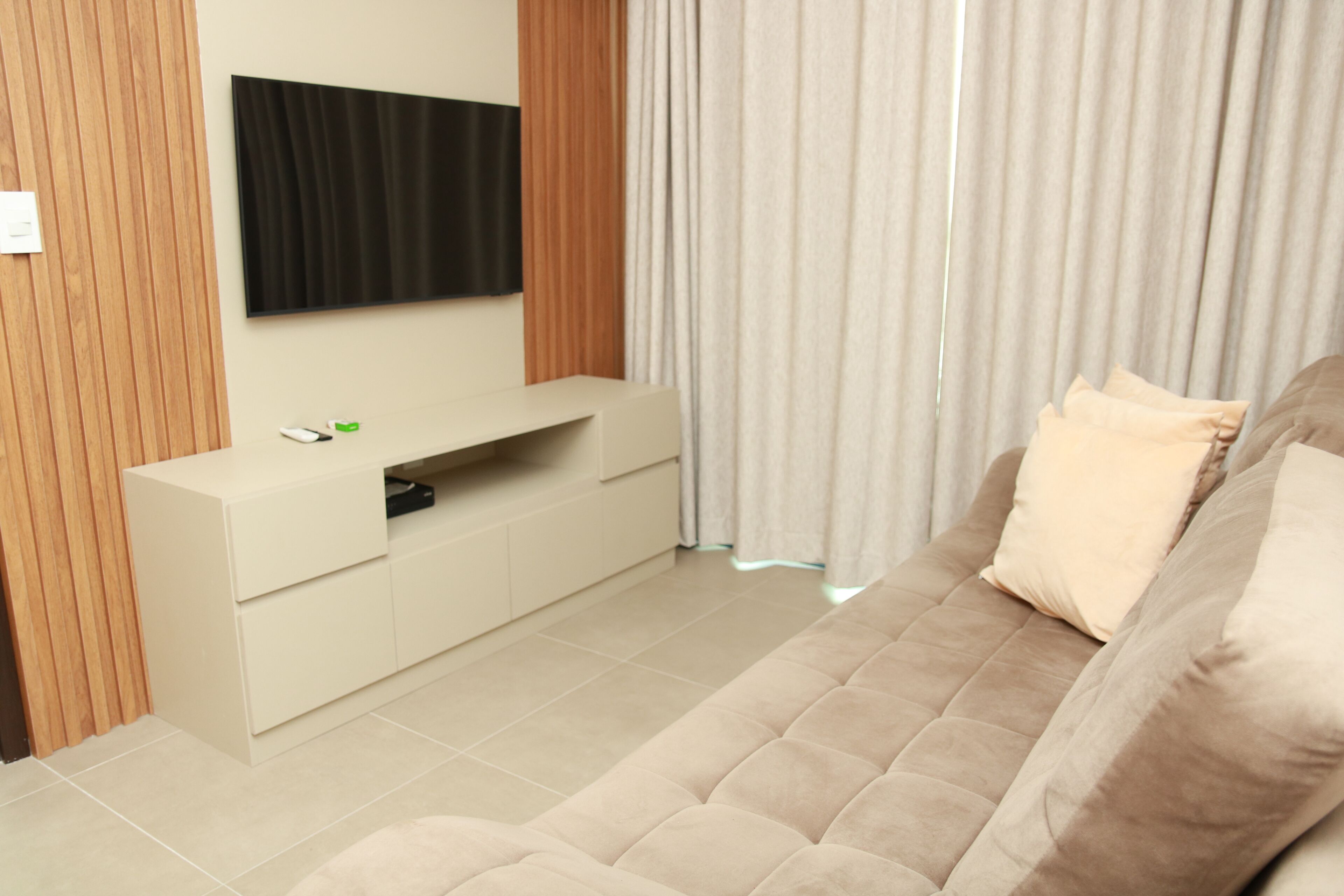 Un salon moderne avec un canapé beige, un téléviseur à écran plat fixé au mur et un panneau en bois sur un des murs.