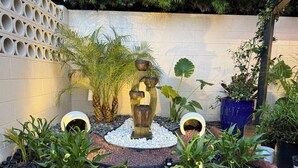 A garden with a water feature, various plants, and a brick wall.