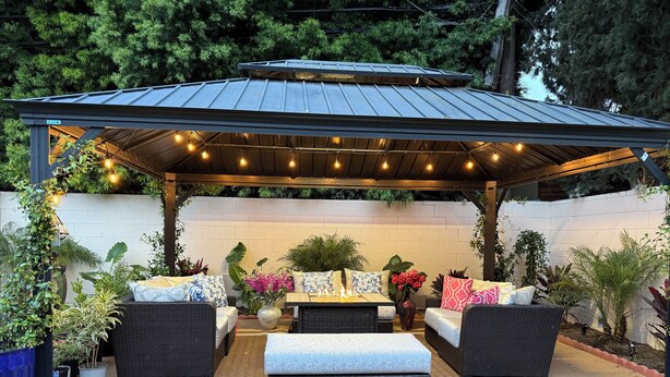 An outdoor patio with a covered seating area, a fire pit, and various potted plants.