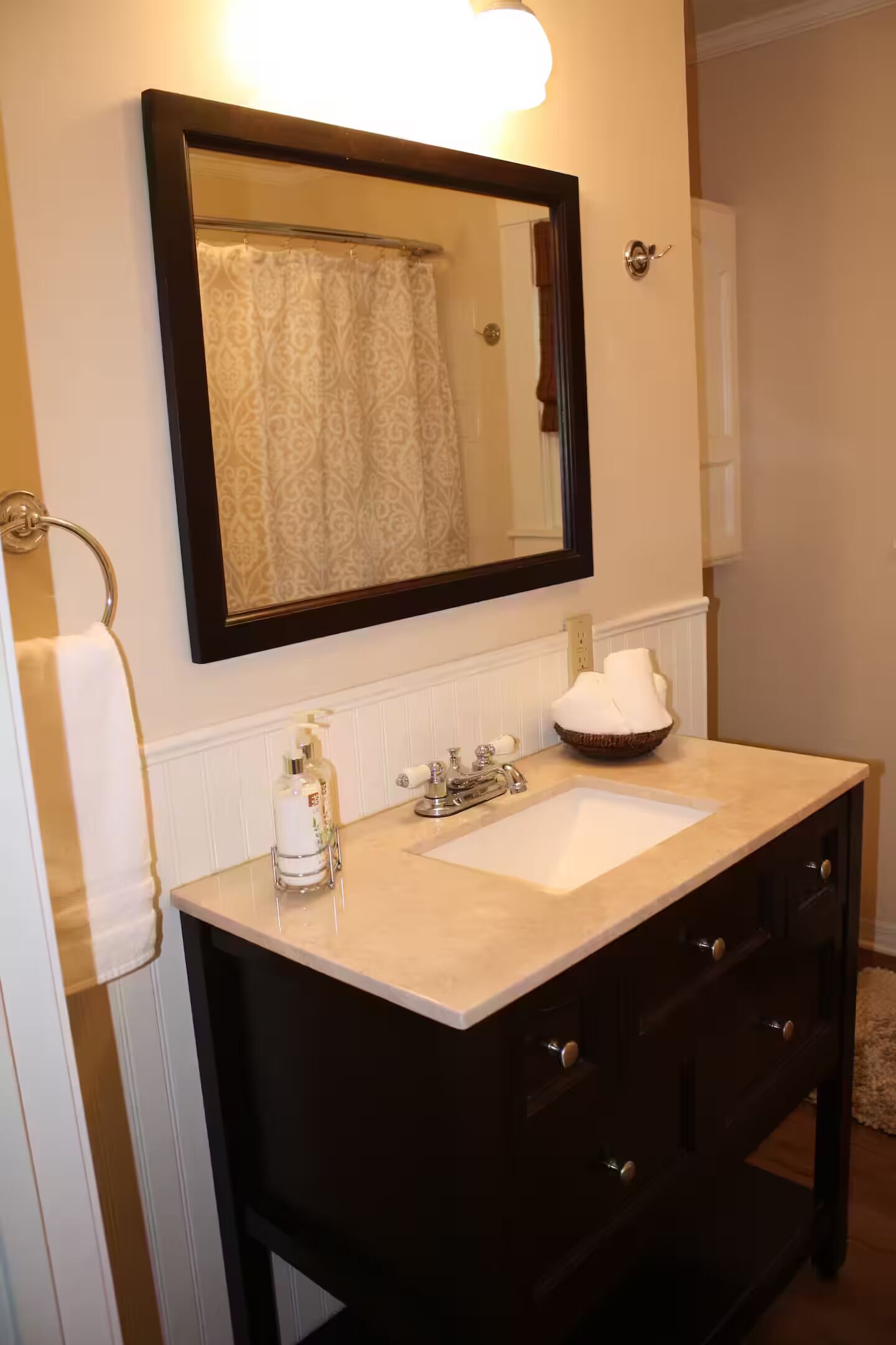 A bathroom with a dark wooden vanity, a white sink, a mirror, and a towel rack.