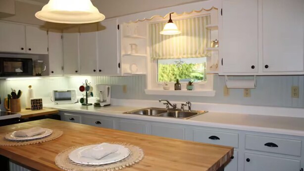 Cocina con armarios blancos, una isla de madera, un fregadero y una ventana con plantas.
