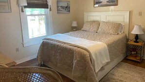 Un dormitorio con una cama, una silla, una mesita de noche, una lámpara y un cuadro en la pared.