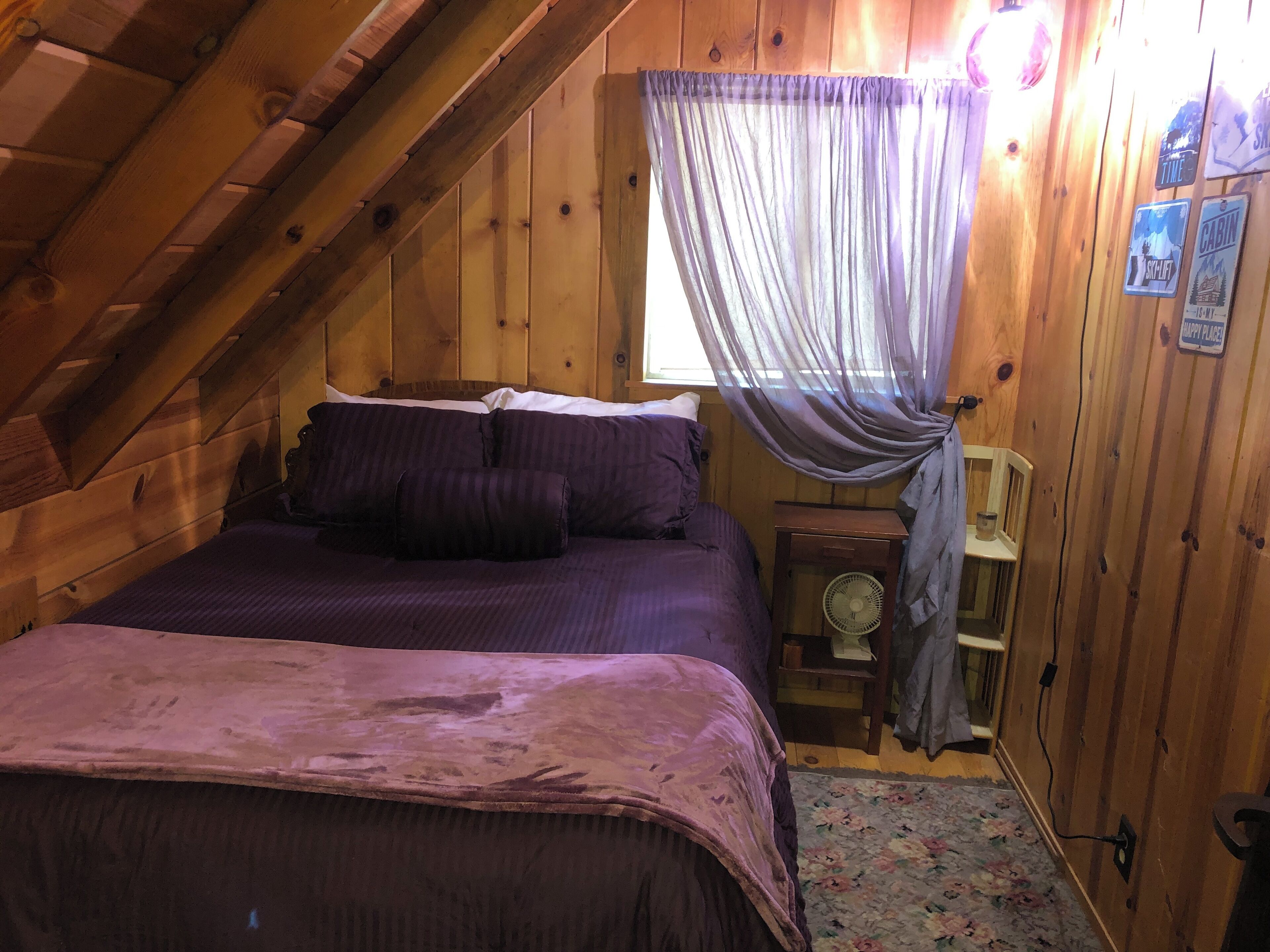 A cozy attic bedroom with a bed, a small table, and a fan.